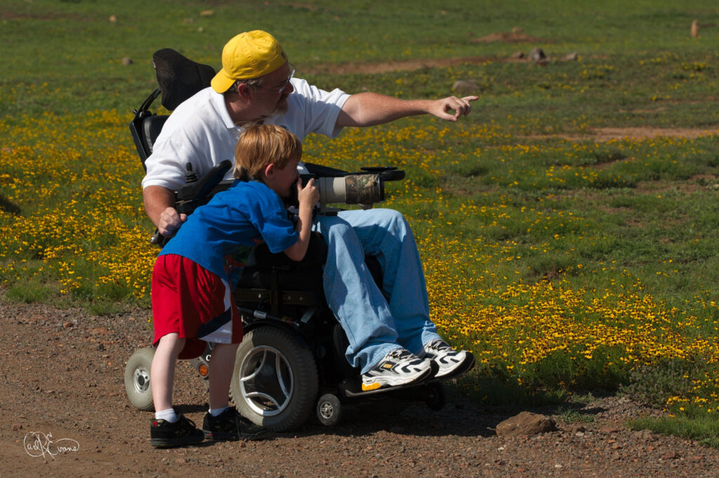 A father teaches his son about photography in a wheelchair at Prairie Dog Town.