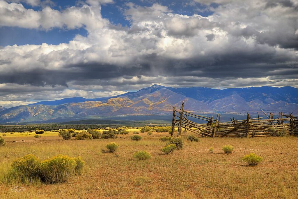 Historic wooden chute frames mountains under a dramatic sky out on the Taos Plateau, New Mexico.