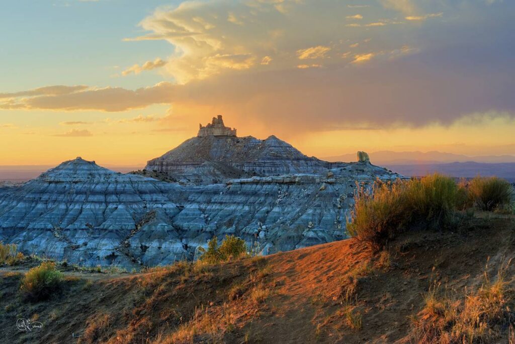 Angel Peak and tiered rock formations in Kutz Canyon, New Mexico, under a golden sunset sky.